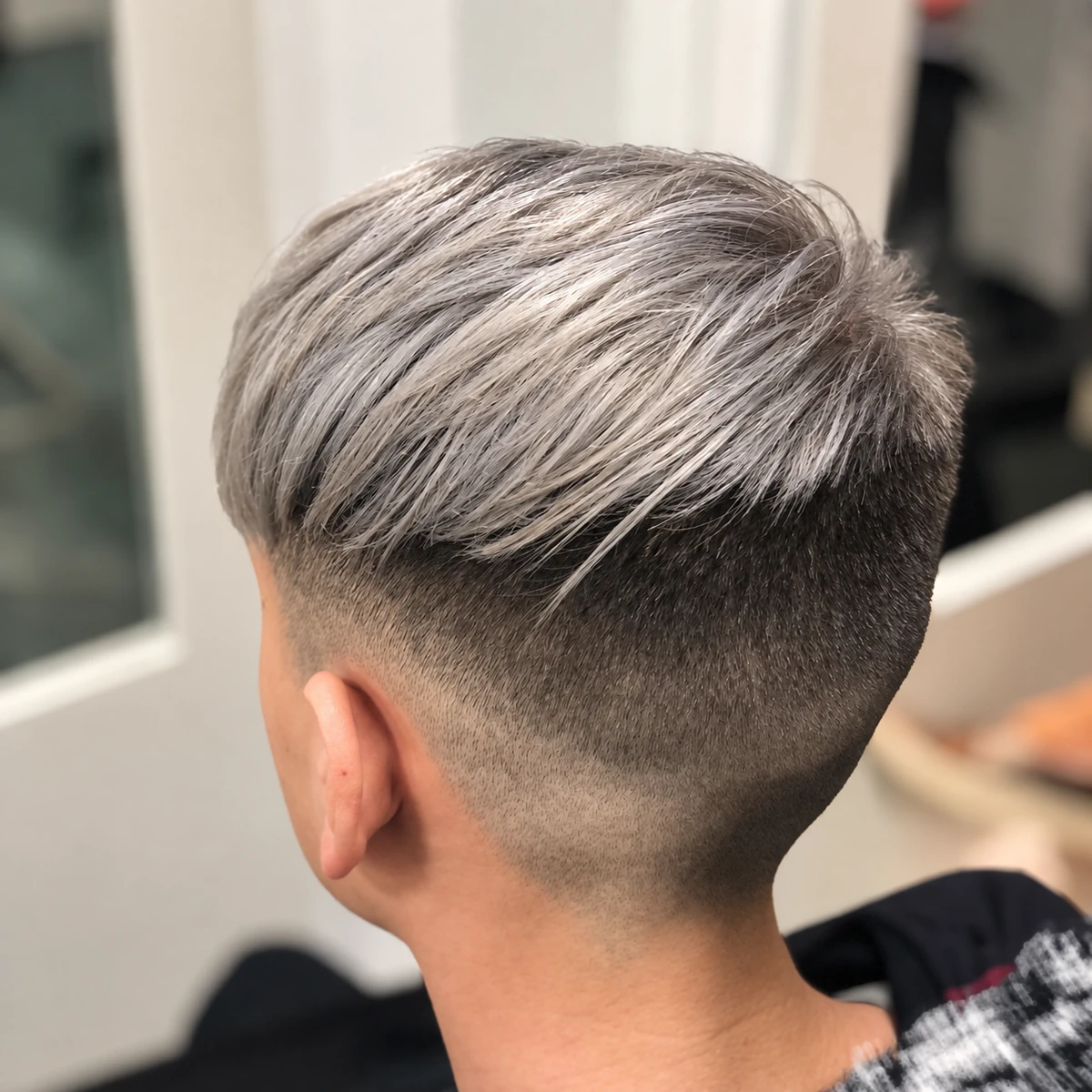 Corte corto con degradado y cabello plateado peinado hacia un lado.